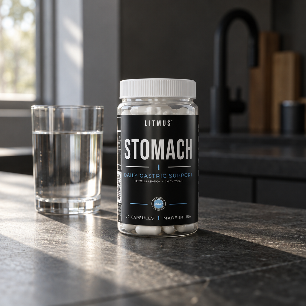 STOMACH capsule jar beside a glass of water on a dark stone kitchen counter in morning sunlight.