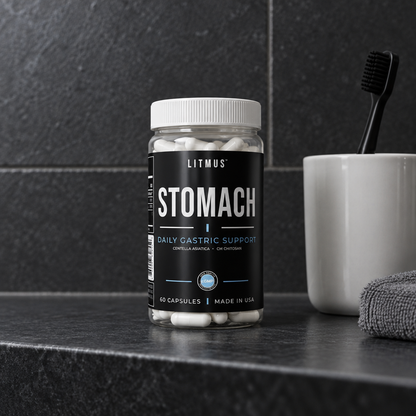 STOMACH supplement jar on a dark tiled bathroom shelf beside a toothbrush cup.