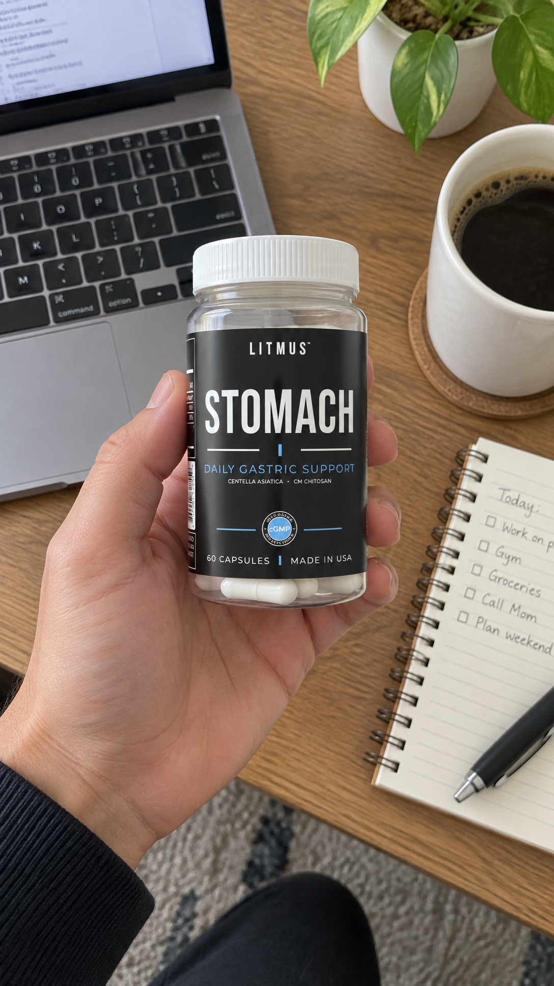 Hand holding a LITMUS STOMACH jar beside a laptop and coffee.