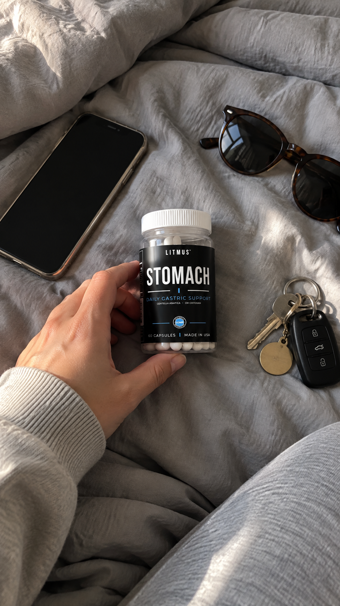 LITMUS STOMACH jar beside everyday carry items on a bed.