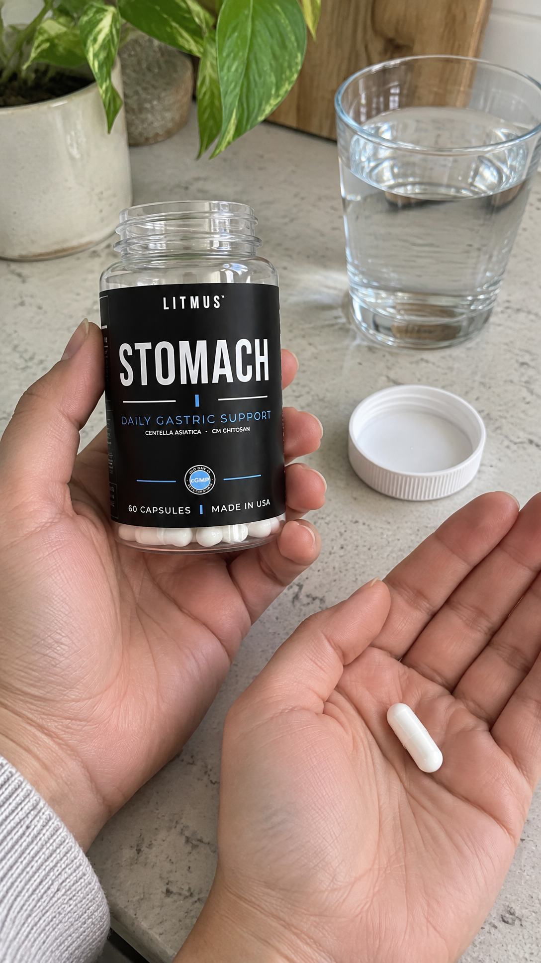 Single white capsule held in front of an open LITMUS STOMACH jar.